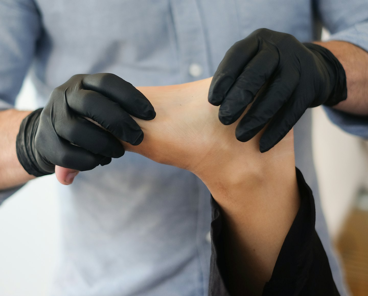 Hände in schwarzen Handschuhen behandeln einen Fuß.